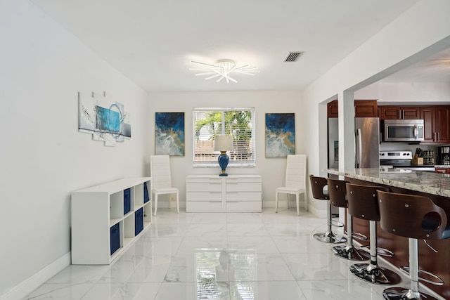 interior space with visible vents, marble finish floor, stainless steel appliances, a breakfast bar area, and baseboards