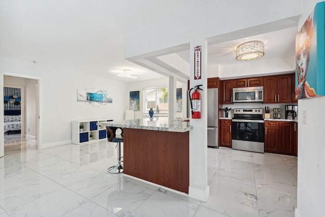 kitchen featuring baseboards, marble finish floor, appliances with stainless steel finishes, and a breakfast bar area