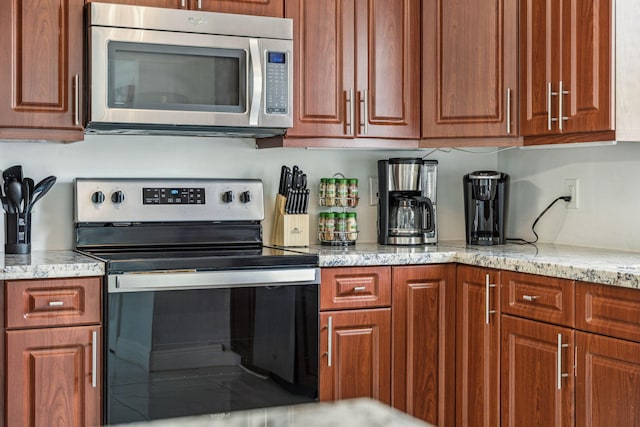 kitchen with stainless steel appliances, light stone countertops, and brown cabinetry