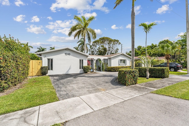 ranch-style house featuring stucco siding, driveway, a front yard, and fence