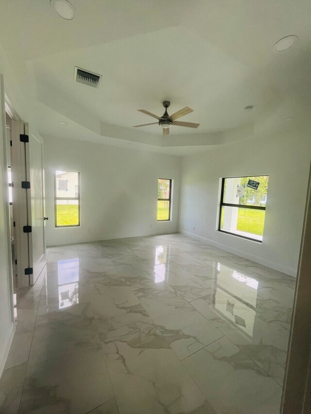 tiled empty room featuring ceiling fan and a raised ceiling