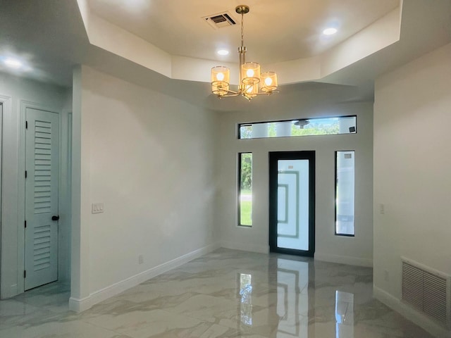 tiled entrance foyer featuring a chandelier and a raised ceiling