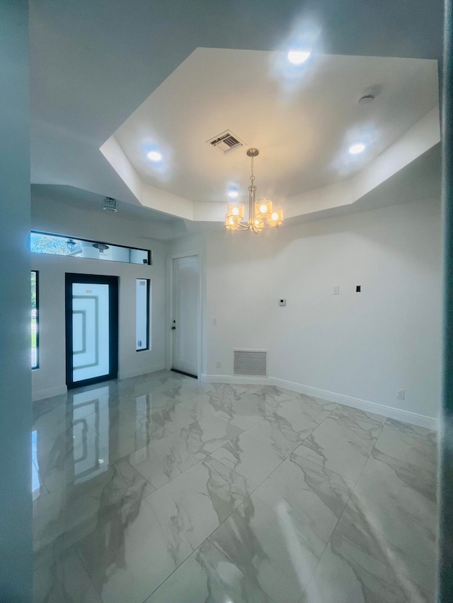 tiled empty room with a tray ceiling and a chandelier