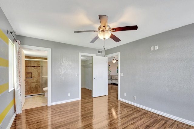 unfurnished bedroom featuring a walk in closet, ensuite bath, a closet, ceiling fan, and light hardwood / wood-style floors