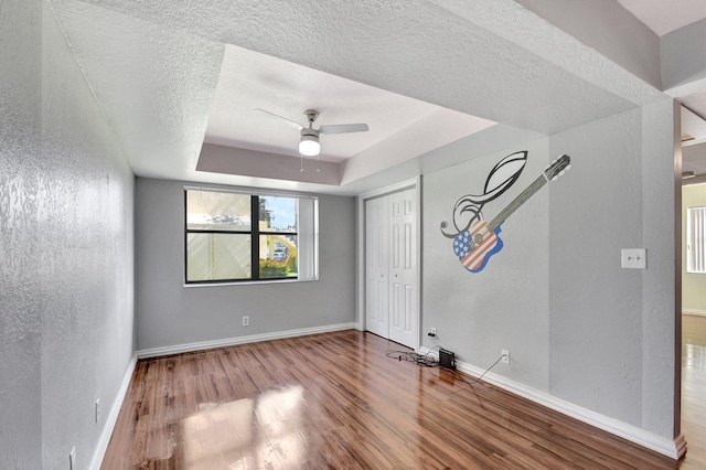 unfurnished bedroom with ceiling fan, hardwood / wood-style floors, a tray ceiling, a textured ceiling, and a closet