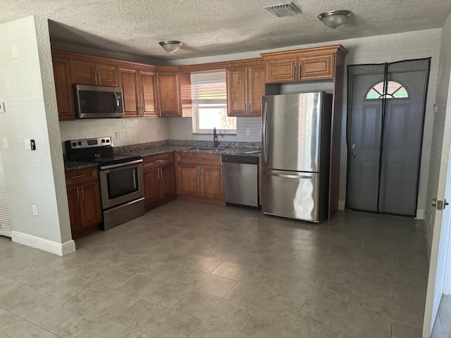 kitchen with light tile patterned flooring, sink, a textured ceiling, appliances with stainless steel finishes, and dark stone countertops