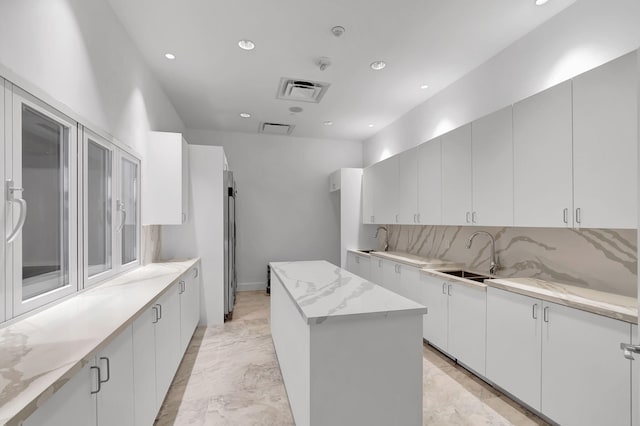 kitchen with tasteful backsplash, sink, light stone countertops, a center island, and white cabinetry