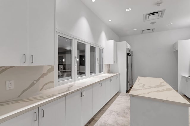 kitchen with light tile patterned floors, white cabinetry, light stone countertops, and a kitchen island