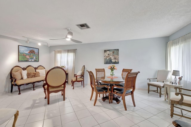 dining space with light tile patterned flooring, ceiling fan, rail lighting, and a textured ceiling