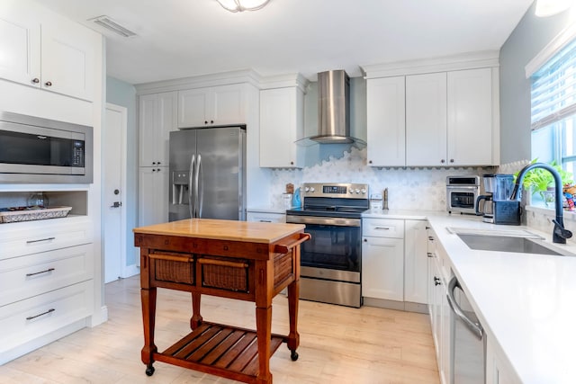 kitchen featuring appliances with stainless steel finishes, light hardwood / wood-style flooring, tasteful backsplash, wall chimney range hood, and sink