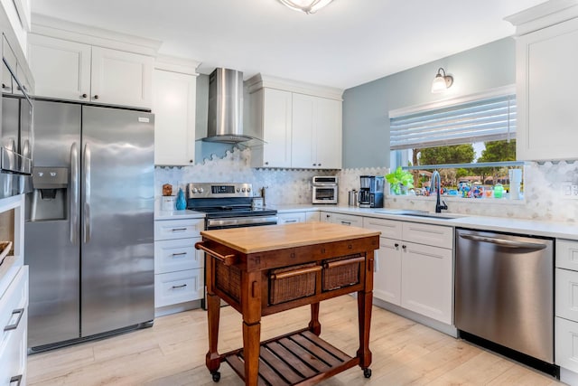 kitchen with wall chimney range hood, white cabinetry, stainless steel appliances, tasteful backsplash, and light wood-type flooring