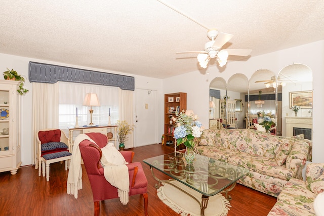 living room with ceiling fan, a textured ceiling, and dark wood-type flooring