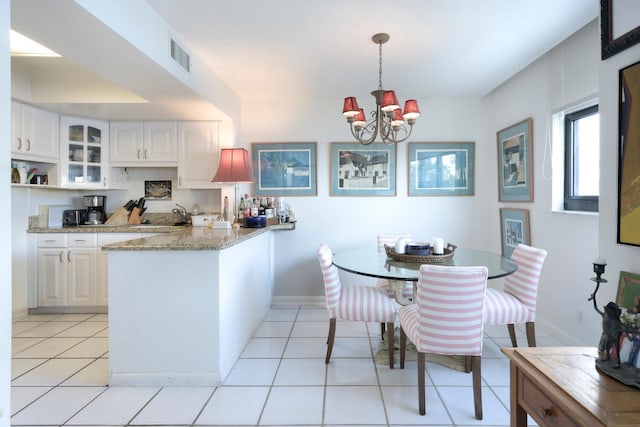 kitchen featuring white cabinets, glass insert cabinets, a peninsula, light stone countertops, and hanging light fixtures