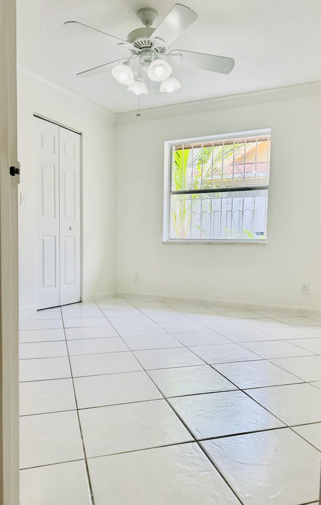 tiled spare room with ceiling fan, baseboards, and crown molding