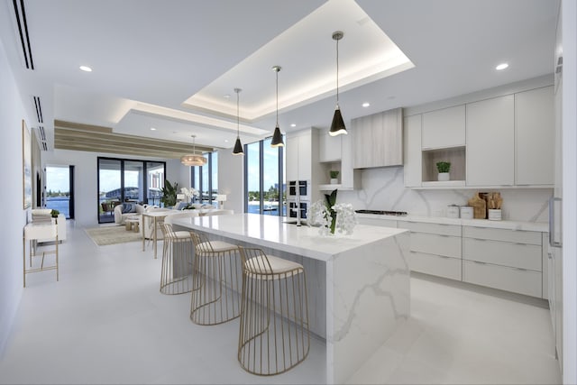 kitchen featuring pendant lighting, white cabinetry, a tray ceiling, and a kitchen island with sink