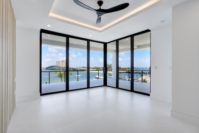 spare room with ceiling fan, plenty of natural light, a raised ceiling, and expansive windows