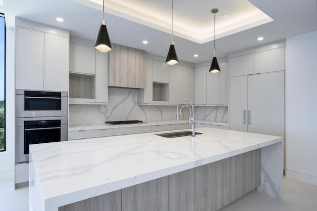 kitchen featuring a kitchen island with sink, sink, a tray ceiling, and pendant lighting