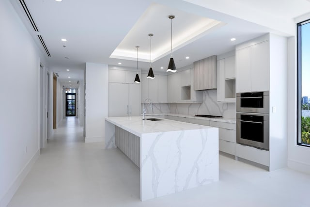 kitchen featuring decorative light fixtures, a spacious island, a raised ceiling, sink, and white cabinets