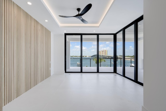 empty room featuring a water view, ceiling fan, floor to ceiling windows, and a raised ceiling