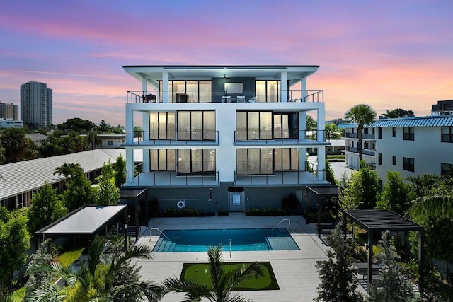 back house at dusk featuring a patio area, a community pool, and a balcony