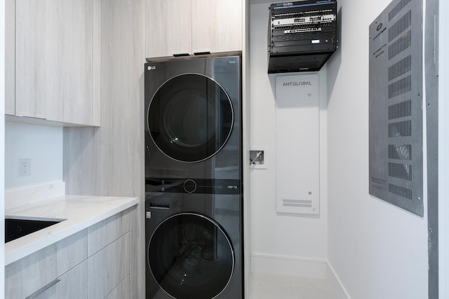 laundry area with cabinets, tile patterned floors, stacked washer / drying machine, and sink