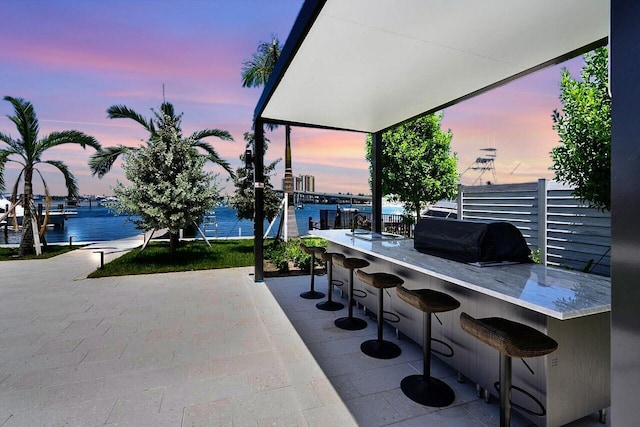 patio terrace at dusk featuring a water view, a bar, and a grill