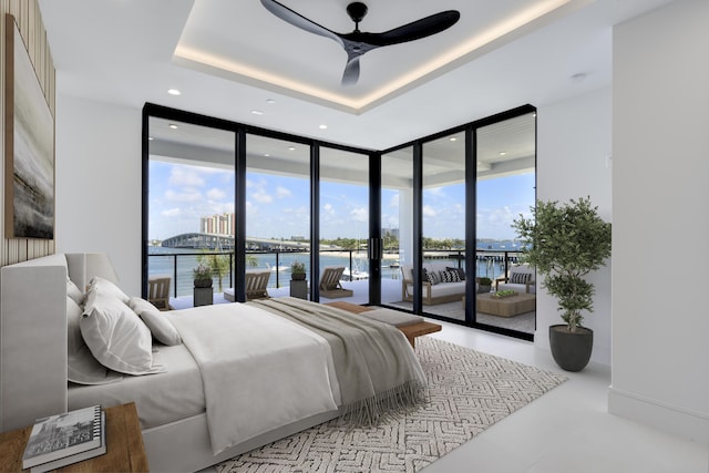 bedroom featuring ceiling fan, a tray ceiling, access to outside, a water view, and expansive windows