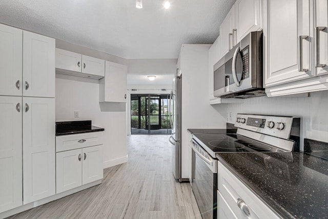 kitchen featuring a textured ceiling, white cabinetry, stainless steel appliances, dark stone countertops, and light hardwood / wood-style flooring