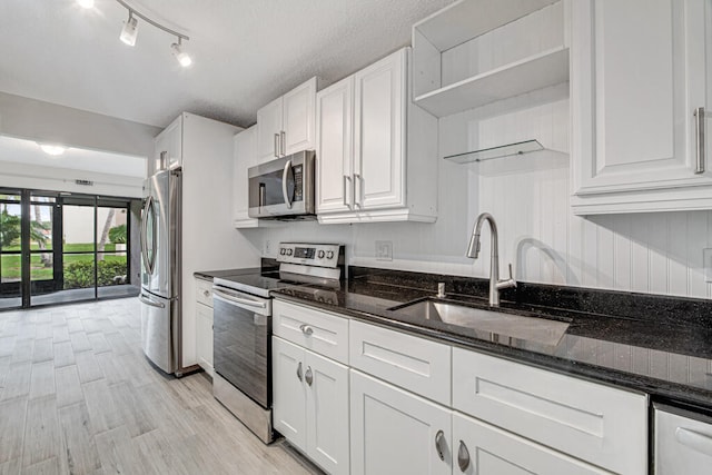 kitchen with white cabinetry, stainless steel appliances, dark stone counters, sink, and light hardwood / wood-style flooring