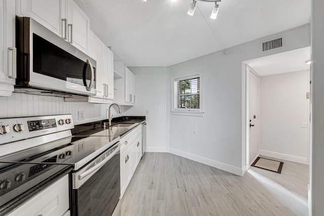 kitchen with light wood-type flooring, appliances with stainless steel finishes, and white cabinets