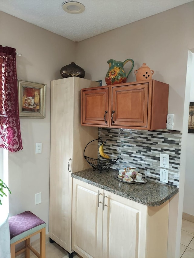 kitchen featuring decorative backsplash, dark stone counters, a textured ceiling, and light tile patterned flooring