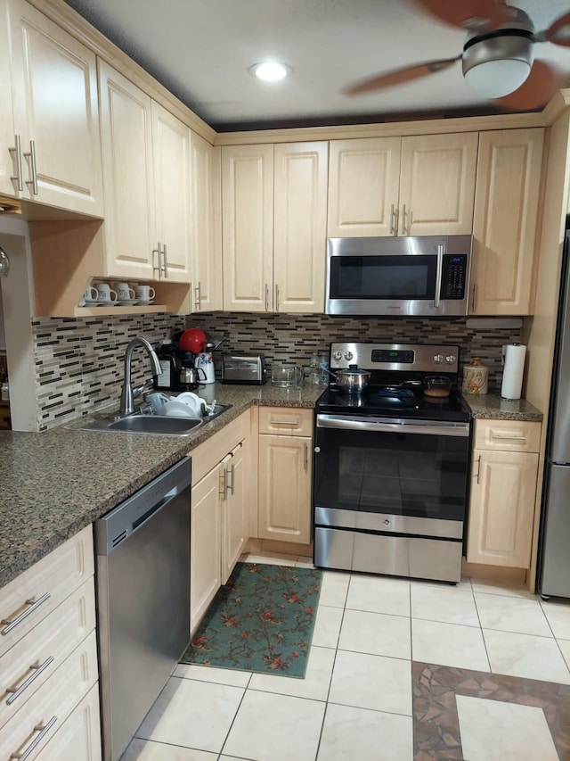 kitchen with sink, ceiling fan, stainless steel appliances, light tile patterned flooring, and dark stone counters