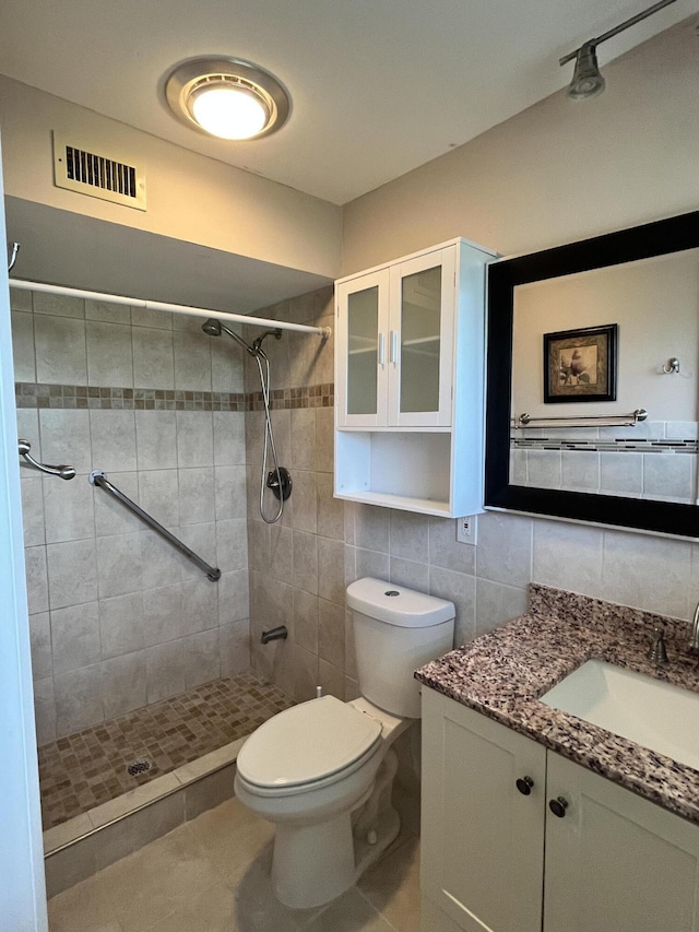 bathroom featuring tiled shower, toilet, tile walls, vanity, and backsplash