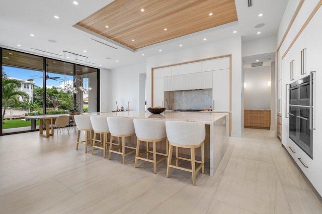 kitchen featuring a large island, white cabinets, wood ceiling, and decorative backsplash