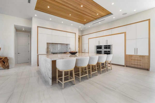 kitchen featuring white cabinetry, a large island, a kitchen breakfast bar, and wooden ceiling