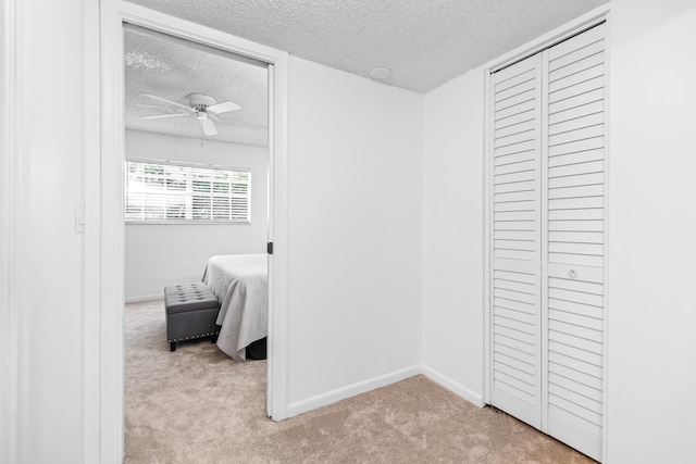 bedroom with ceiling fan, light colored carpet, a textured ceiling, and a closet