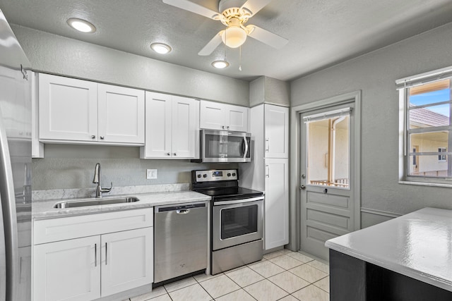 kitchen with light tile patterned floors, stainless steel appliances, a textured wall, white cabinetry, and a sink