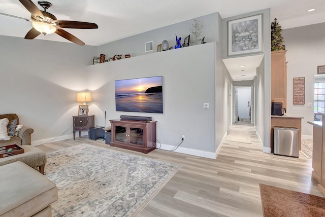 living room with ceiling fan, a high ceiling, and light wood-type flooring