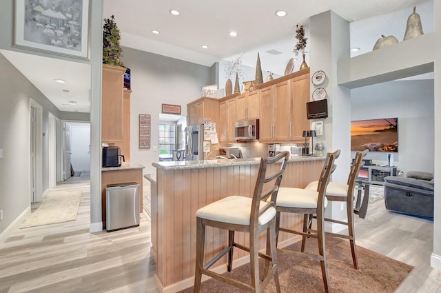 kitchen featuring light hardwood / wood-style flooring, stainless steel appliances, a kitchen bar, light brown cabinetry, and kitchen peninsula