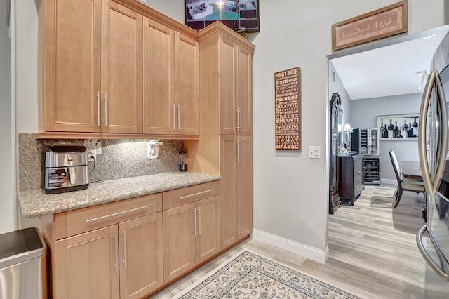 kitchen featuring stainless steel refrigerator, tasteful backsplash, beverage cooler, light stone counters, and light wood-type flooring