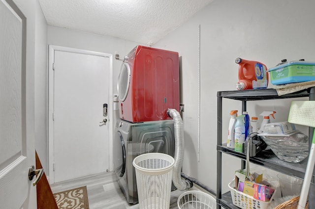 laundry area featuring light hardwood / wood-style flooring, a textured ceiling, and stacked washing maching and dryer