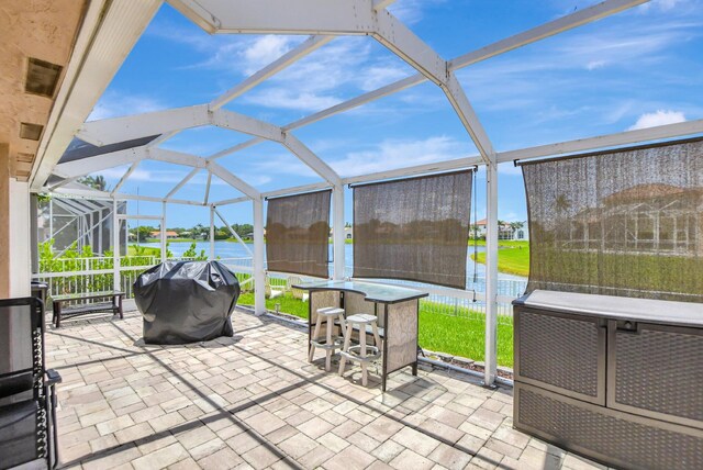 view of patio / terrace with a grill, a water view, an outdoor bar, and glass enclosure