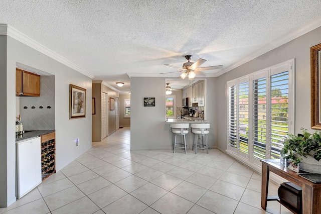 kitchen with light tile patterned floors, kitchen peninsula, a kitchen breakfast bar, dishwasher, and crown molding