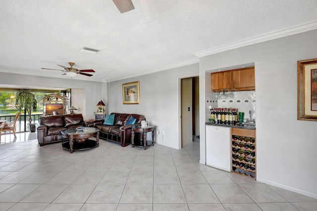 tiled living room with indoor wet bar, ceiling fan, a textured ceiling, and ornamental molding