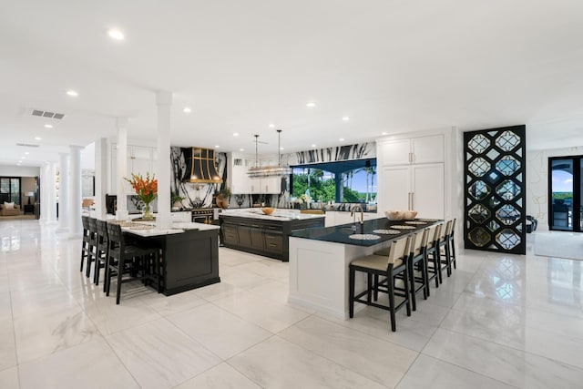 kitchen with white cabinetry, a kitchen bar, decorative light fixtures, and ornate columns