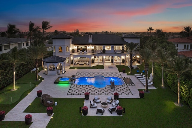 pool at dusk featuring a gazebo, an in ground hot tub, an outdoor living space with a fire pit, a patio area, and a lawn