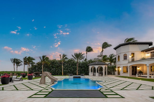 pool at dusk featuring a gazebo, a water slide, and a patio area