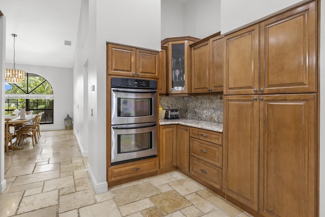 kitchen with stainless steel double oven, an inviting chandelier, tasteful backsplash, light stone counters, and pendant lighting