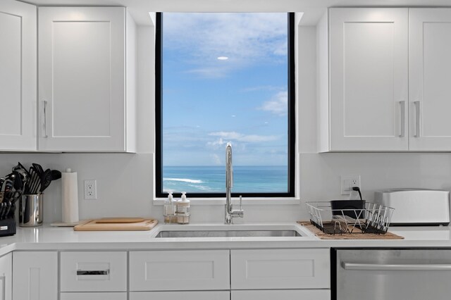 kitchen featuring sink, stainless steel dishwasher, white cabinetry, and a water view