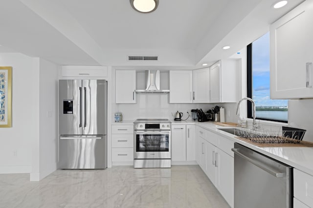 kitchen with stainless steel appliances, sink, light tile patterned floors, white cabinetry, and wall chimney exhaust hood